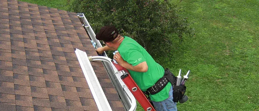 Leaning in from a red ladder to work along a white gutter run