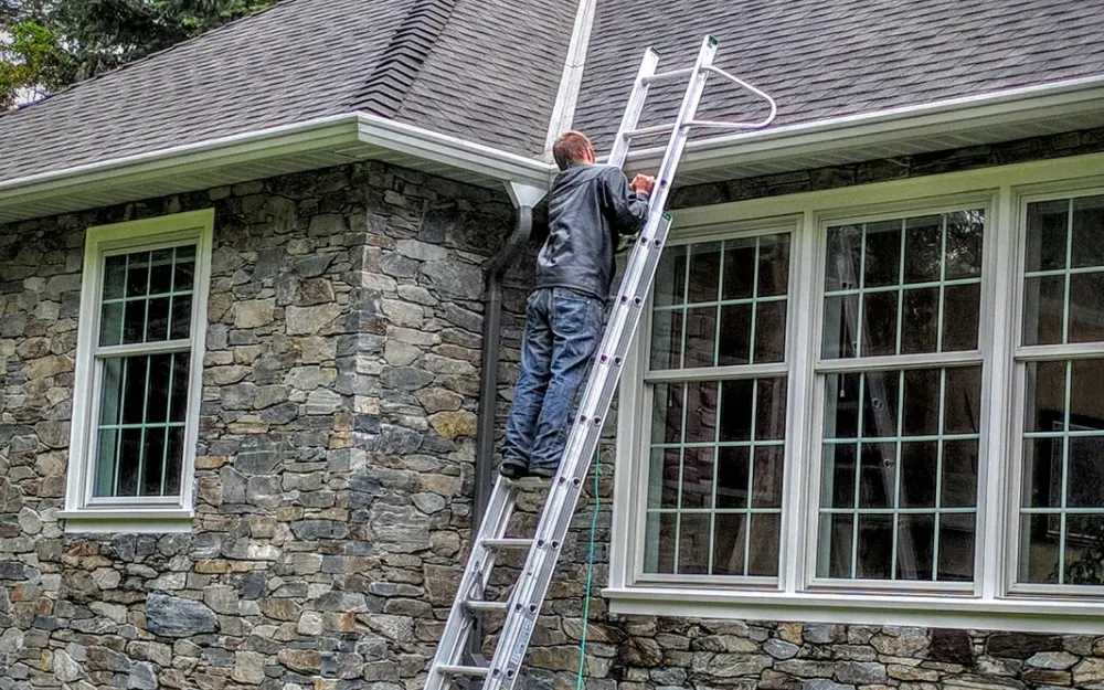 An extension ladder against a stone house, working at the gutter by the downspout